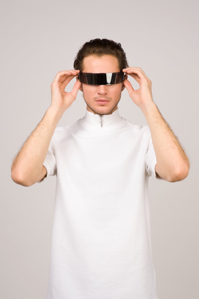 A young man in a stylish white shirt poses with futuristic VR glasses, embodying modern tech fashion.